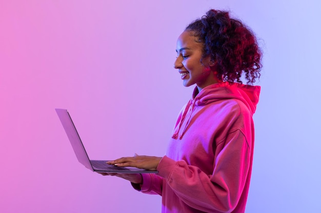 Mujer negra alegre con una computadora portátil en un fondo de neón colorido