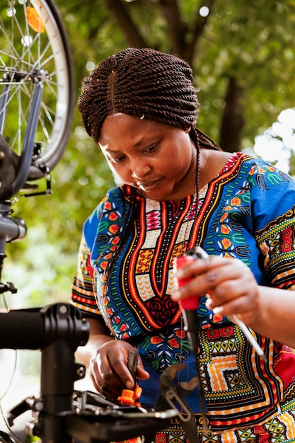 Mujer negra amante de los deportes que repara y ajusta componentes de bicicletas con herramientas de trabajo expertas para el mantenimiento anual de verano. Mujer afroamericana sana que examina el juego de herramientas y repara la bicicleta.