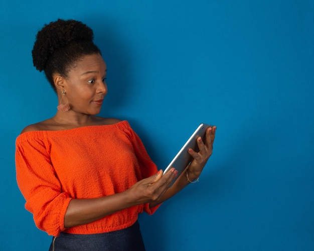 Mujer negra asustada sosteniendo una tableta en sus manos con una pared azul