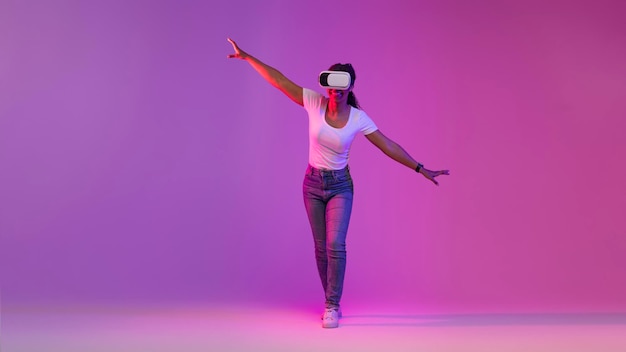 Mujer negra en auriculares VR explorando actividades del ciberespacio caminando en luz de neón