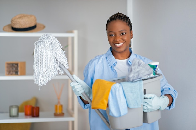 Mujer negra bastante joven alegre que sostiene las herramientas de limpieza
