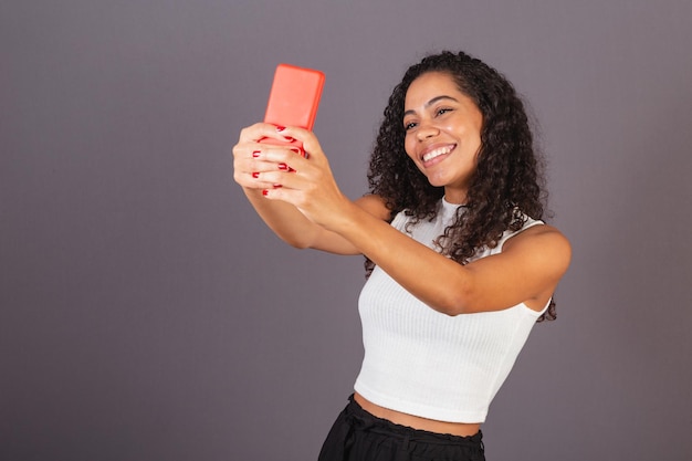 Mujer negra brasileña joven que toma el autorretrato del selfie con el teléfono celular rojo