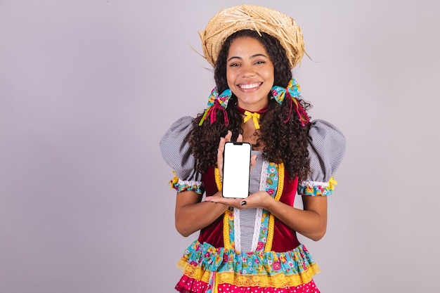 Mujer negra brasileña con ropa de fiesta de junio fraternización en nombre de Sao Joao Arraial con smartphone y pantalla para textos y anuncios