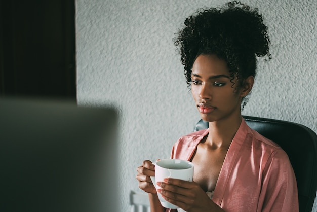 Mujer negra en casa trabajando con computadora y café en la mañana