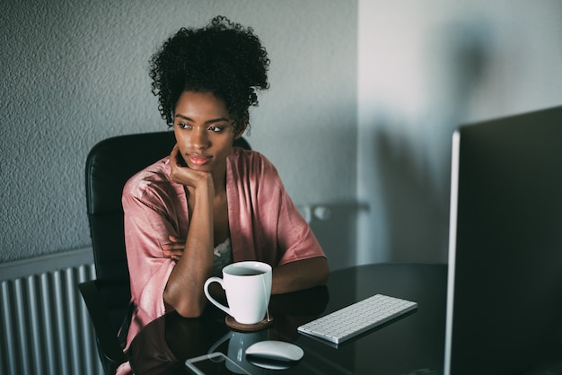 Mujer negra en casa trabajando con computadora y café en la mañana