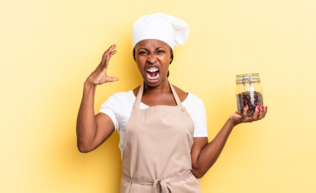 Mujer negra chef afro gritando con las manos en el aire, sintiéndose furiosa, frustrada, estresada y molesta. concepto de granos de cafe