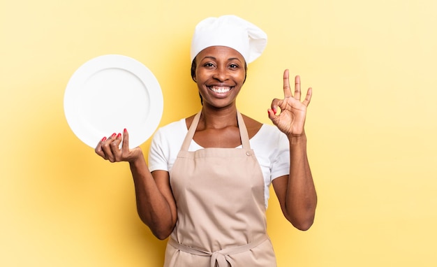 Mujer negra chef afro que se siente feliz, relajada y satisfecha, mostrando aprobación con gesto bien, sonriendo. concepto de plato vacío