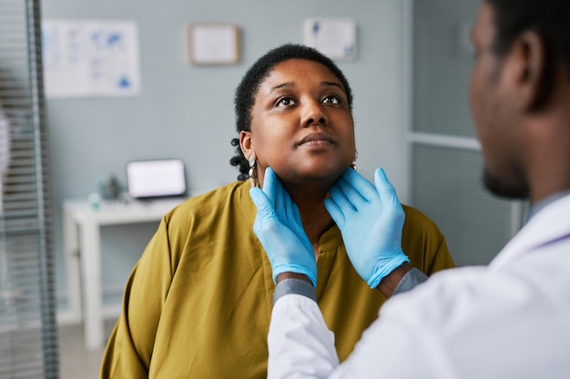 Mujer negra en el chequeo médico con el médico palpando el cuello