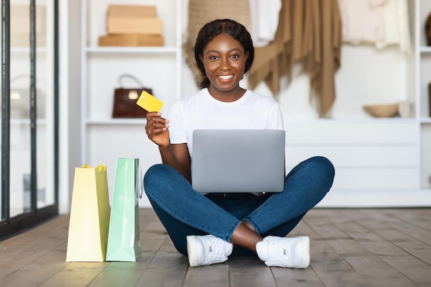 Mujer negra comprando en línea usando una computadora portátil y una tarjeta de crédito en interiores
