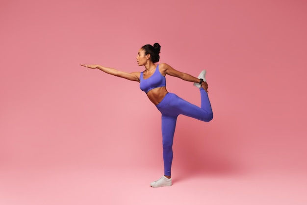 Mujer negra deportiva practicando ejercicio de equilibrio estirando la pierna levantada en el estudio