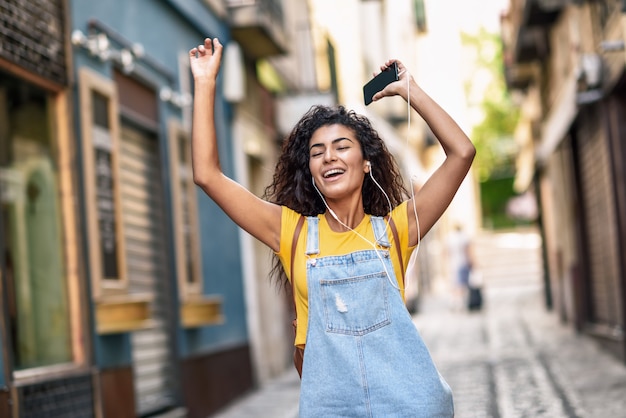 Mujer negra divertida que escucha la música con los auriculares al aire libre.