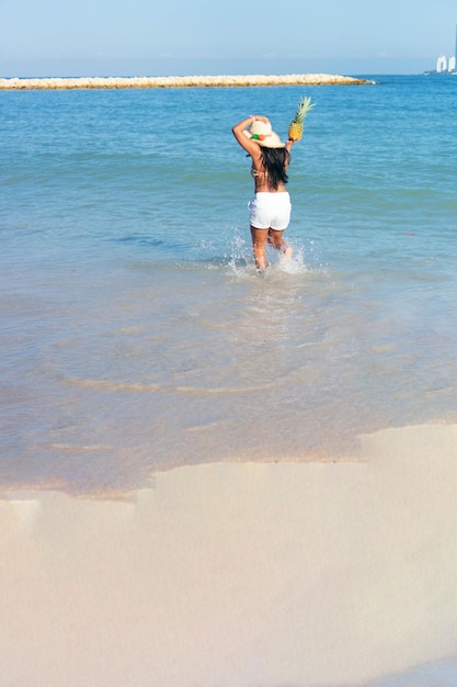 Mujer negra se divierte en la playa con una piña en sus manos.