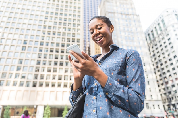 Mujer negra escribiendo en el teléfono en la ciudad