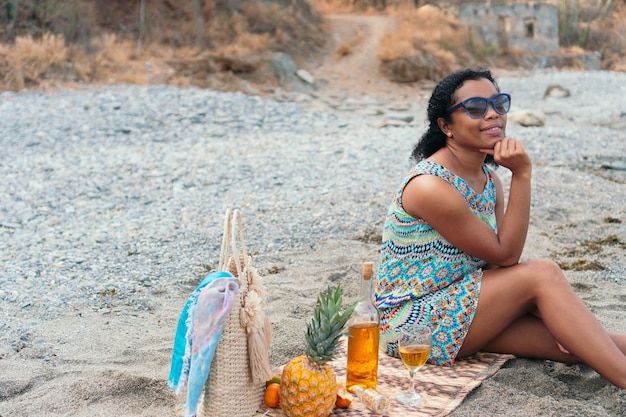 Mujer negra está sentada en la playa con una copa de vino en las vacaciones de verano