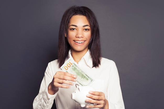 Mujer negra exitosa poniendo en la alcancía un billete de cien dólares