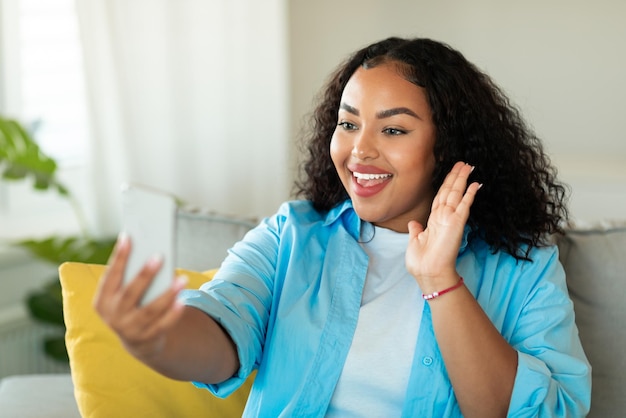 Mujer negra feliz haciendo videollamadas por teléfono en casa