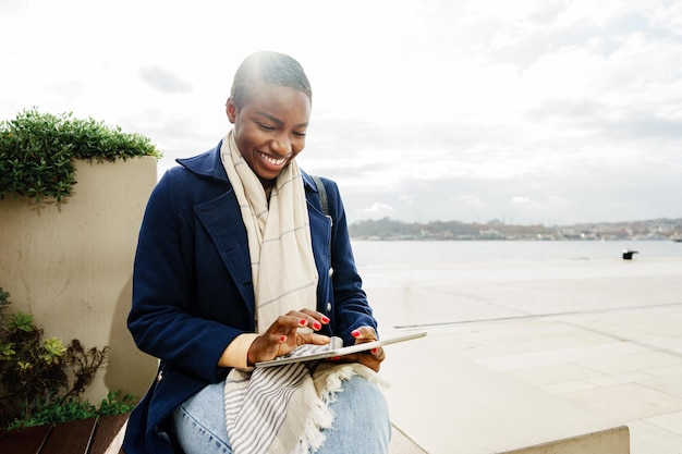 Mujer negra feliz usando una tableta digital al aire libre