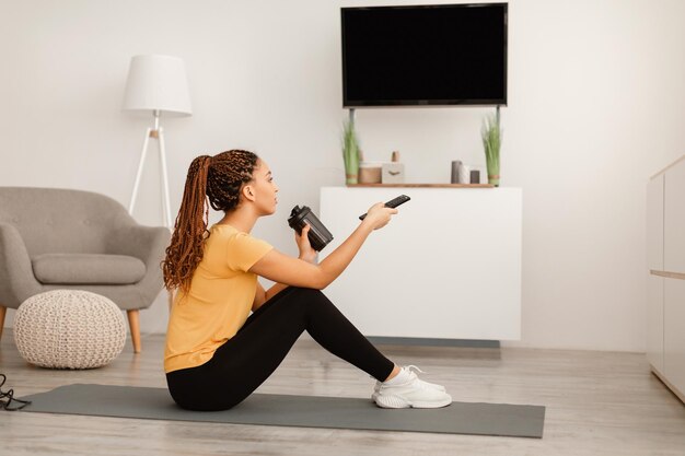 Mujer negra en forma bebiendo café viendo la televisión sentada en casa