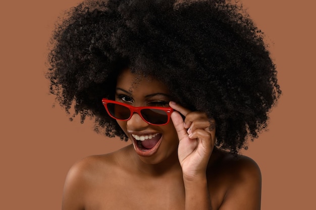 mujer negra con gafas de sol y parpadea sobre las gafas en un fondo beige