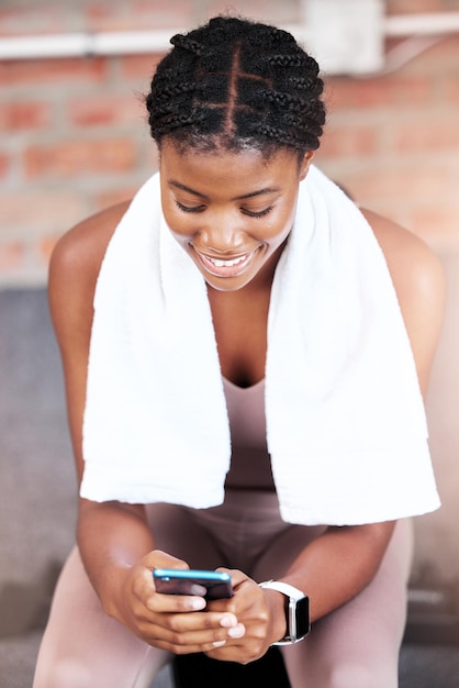 Mujer negra en el gimnasio y sonríe con las redes sociales del teléfono o chateando en la aplicación web o en Internet en un descanso del entrenamiento.