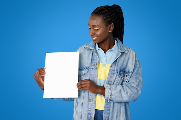 Mujer negra joven alegre que muestra el cartel en blanco en azul