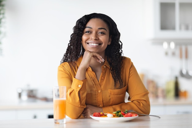 Mujer negra joven feliz que tiene el interior adecuado de la cocina del desayuno