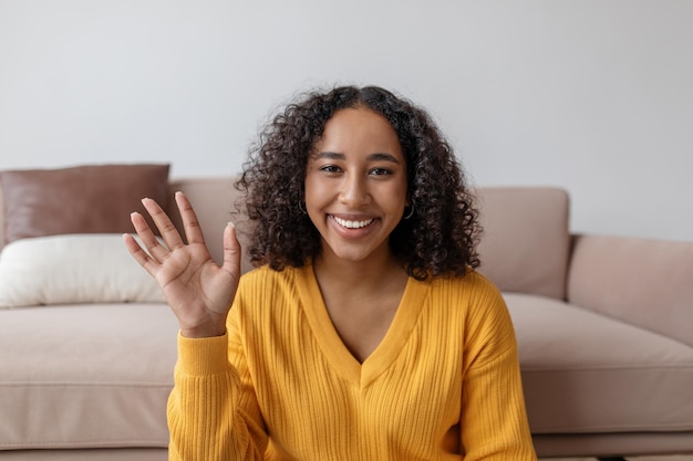 Mujer negra joven positiva saludando a la cámara web hablando con familiares o amigos en una computadora portátil desde casa