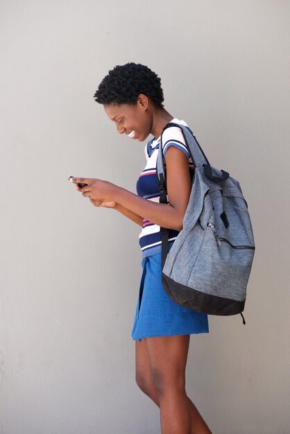 Mujer negra joven que camina y que usa el teléfono celular en fondo gris