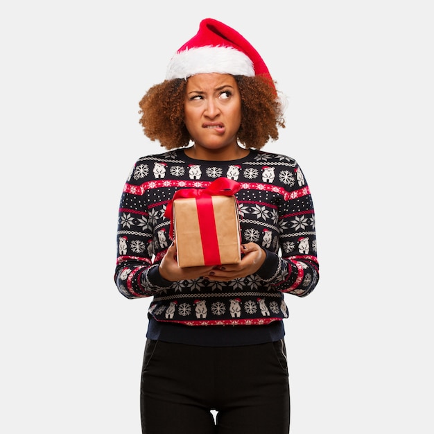 Mujer negra joven que sostiene un regalo en el día de Navidad que piensa en una idea