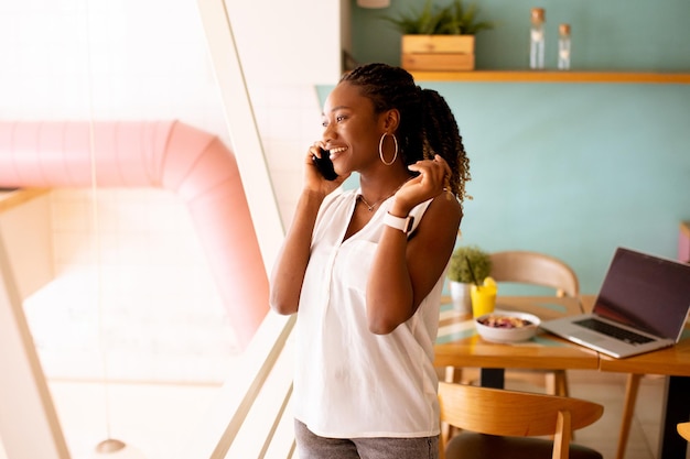 Mujer negra joven que usa el teléfono móvil en el café