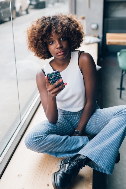 Mujer negra joven con el smartphone que mira la cámara