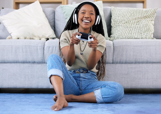 Mujer negra jugando y sonriendo con el controlador junto al sofá de la sala para un partido divertido o un juego en línea en casa Mujer afroamericana feliz jugando videojuegos con auriculares para entretenimiento o deportes electrónicos