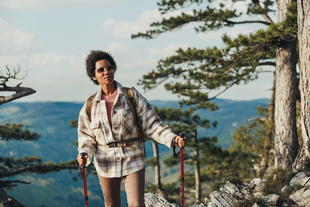 Mujer negra madura parada en la cima de una colina y disfrutando de la vista durante su caminata en las montañas.