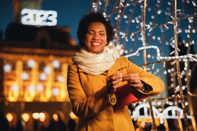 Mujer negra de mediana edad sosteniendo bengalas en la noche festiva de invierno en la ciudad.