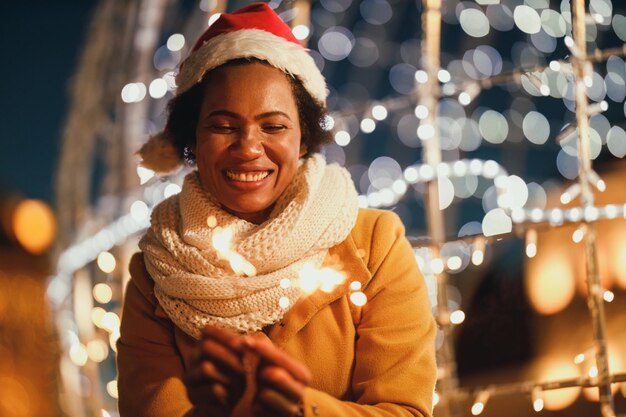 Mujer negra de mediana edad sosteniendo bengalas en la noche festiva de invierno en la ciudad.