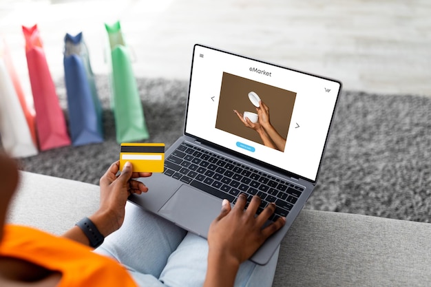 Mujer negra milenaria que usa una computadora portátil con crema en la pantalla y una tarjeta de crédito hace un pedido en línea