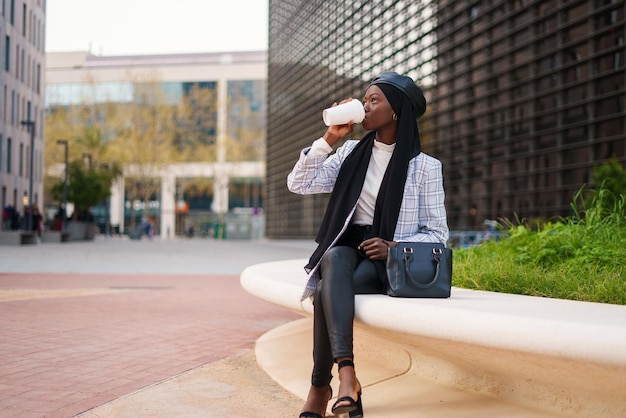 Mujer negra de moda bebiendo café para llevar en un banco