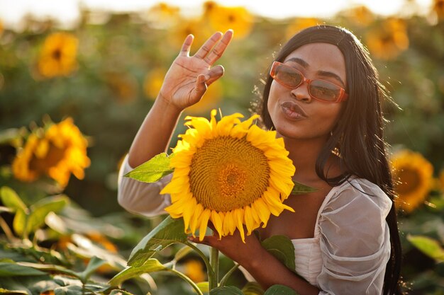 Una mujer negra muy joven usa una pose de vestido de verano en un campo de girasoles.