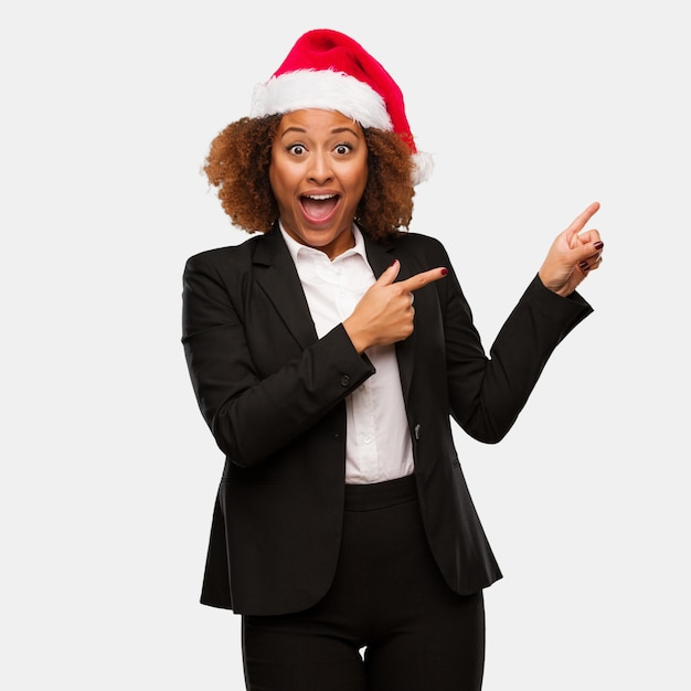 Mujer negra del negocio joven que lleva un sombrero de santa de los chirstmas que lleva a cabo algo con la mano