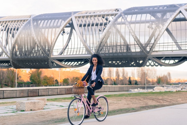 Mujer negra de negocios andar en bicicleta vintage en la ciudad