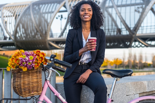 Mujer negra de negocios con bicicleta vintage bebiendo café