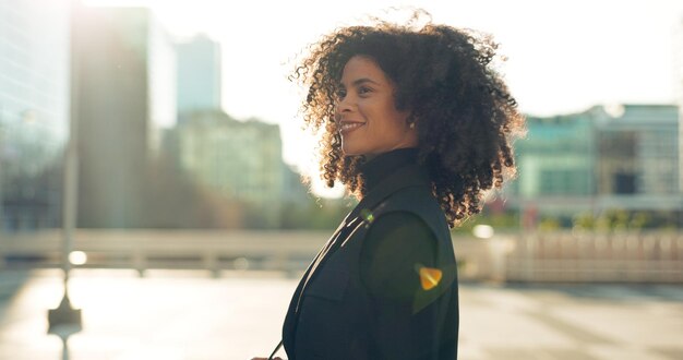 Mujer negra de negocios y caminando al aire libre en el edificio de la ciudad con pensamiento y sonrisa para el viaje de la mañana o viaje al aire libre persona feliz con afro y trabajador corporativo moviéndose a trabajar en la ciudad urbana