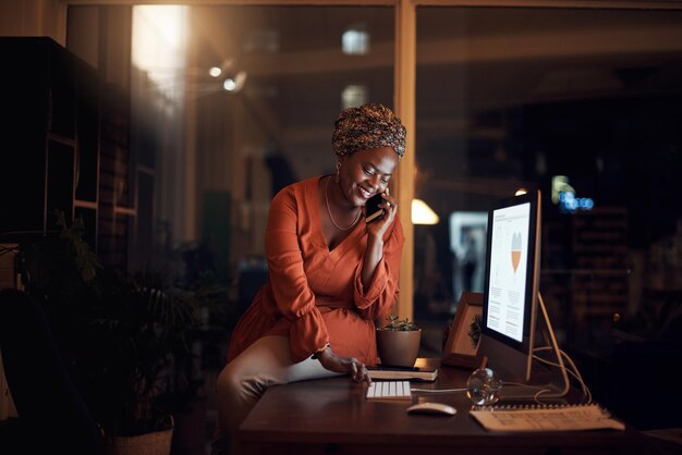 Mujer negra de negocios y llamada telefónica en la computadora del teléfono inteligente escribiendo y conversando por la noche Teléfono celular de trabajador feliz y comunicación para la red móvil de administración de escritorio y horas extra en la oficina