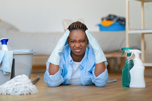 Mujer negra nerviosa irritada tirada en el suelo mientras hacía las tareas del hogar