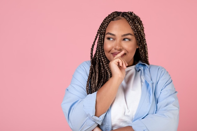 Mujer negra obesa feliz soñando mirando a un lado sobre fondo rosa