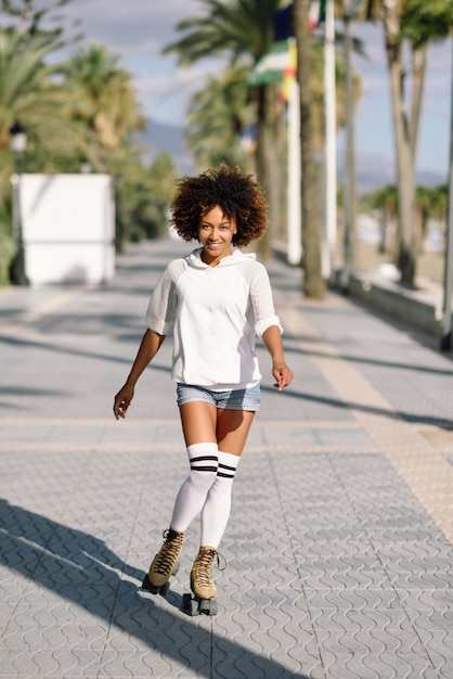 Mujer negra en patines patinar en el paseo de la playa con palmeras