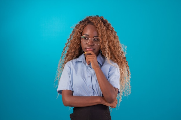 Mujer negra con pelo rizado en foto de estudio con camisa azul y falda negra y haciendo varias expresiones faciales.