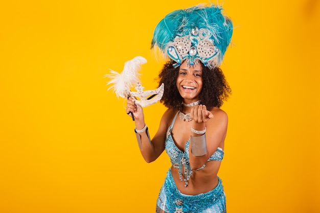 Mujer negra reina de la escuela de samba brasileña con ropa de carnaval azul y corona de plumas con máscara invitando a las manos