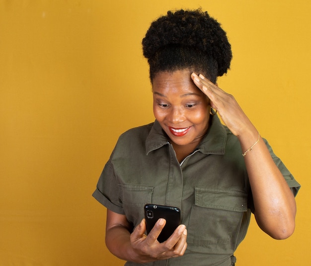 Mujer negra en ropa verde sosteniendo un teléfono celular sobre una superficie amarilla