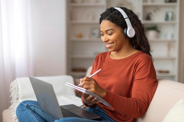 Mujer negra sentada en el sofá con computadora portátil y auriculares